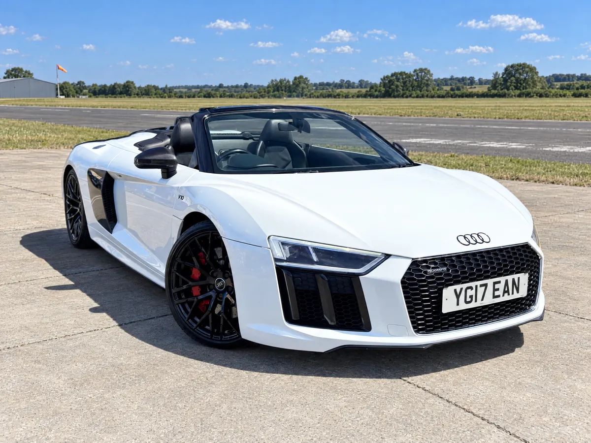 Close front three-quarter view of the Audi R8 Spyder, roof down, carbon mirror and headlight detail